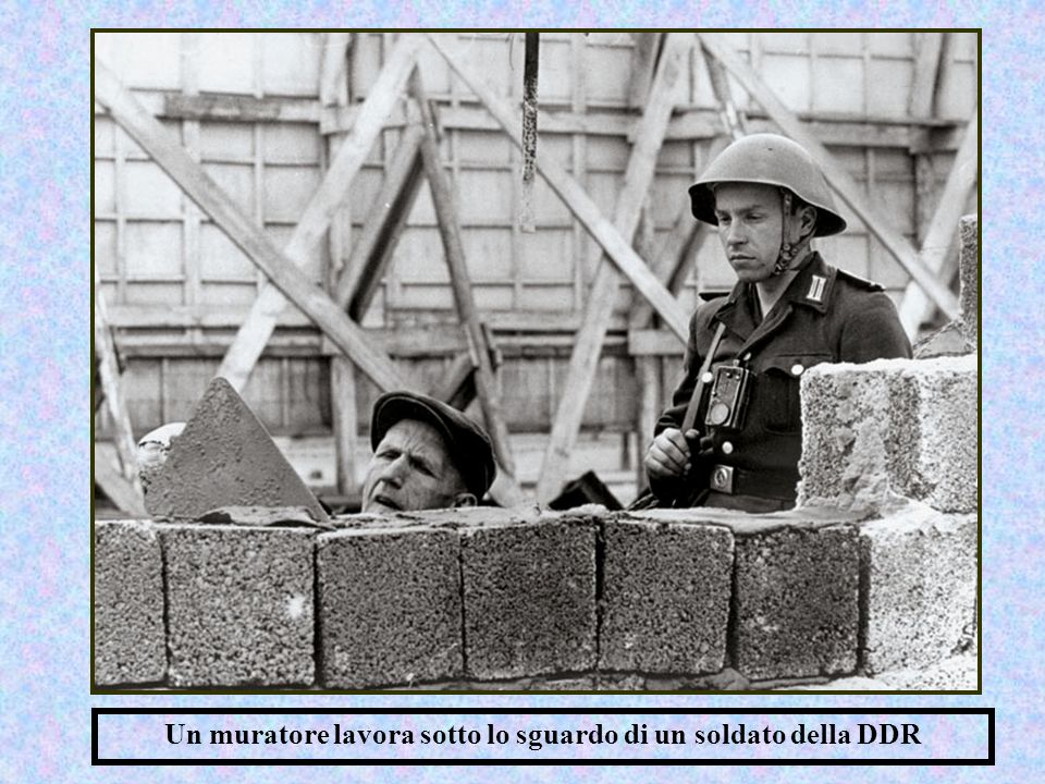 Un muratore lavora sotto lo sguardo di un soldato della DDR